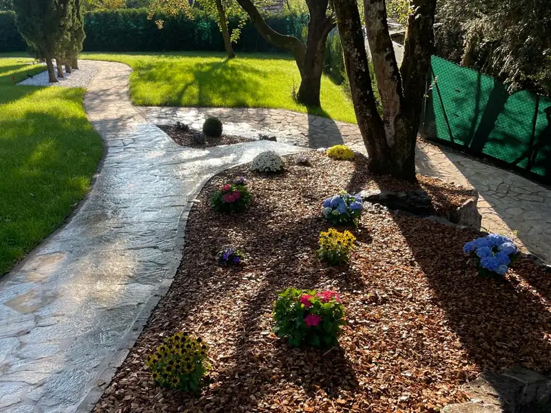 Allée en pierre naturelle bordée d'un massif paillé et fleuri, jardin privé entretenu par H Bat Sàrl