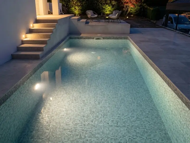 Piscine construite par H Bat Sàrl, en eau et éclairée, avec sa plage en dalles claires