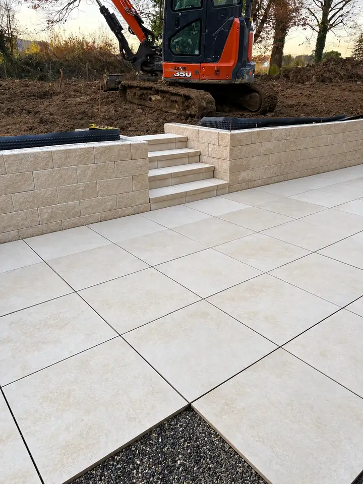 Terrasse en dalles grand format avec muret de soutènement et escalier en pierre reconstituée